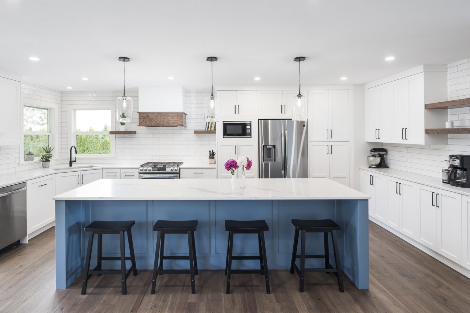 Custom kitchen by Alderidge Construction with white perimeter cabinetry, slate blue island with waterfall countertop, pendant lights, and bar stool seating