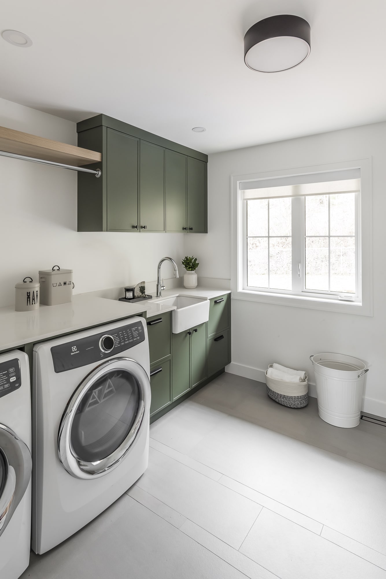 Custom laundry room by Alderidge Construction with olive green shaker cabinetry, farmhouse sink, and stacked washer-dryer alcove for efficient home organization