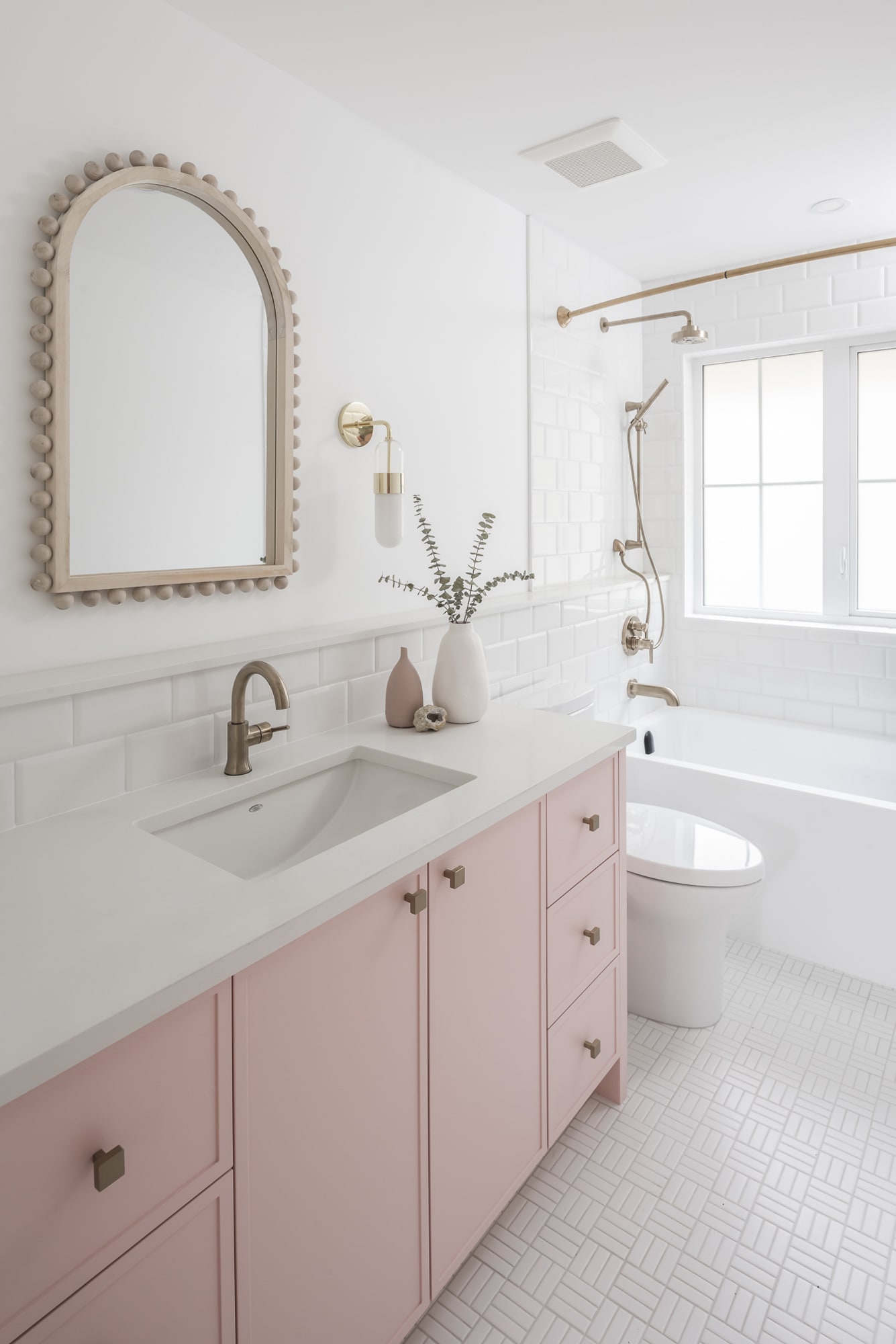 Custom blush pink bathroom vanity cabinetry by Alderidge Construction with decorative beaded oval mirror and white quartz countertop in a feminine bathroom design
