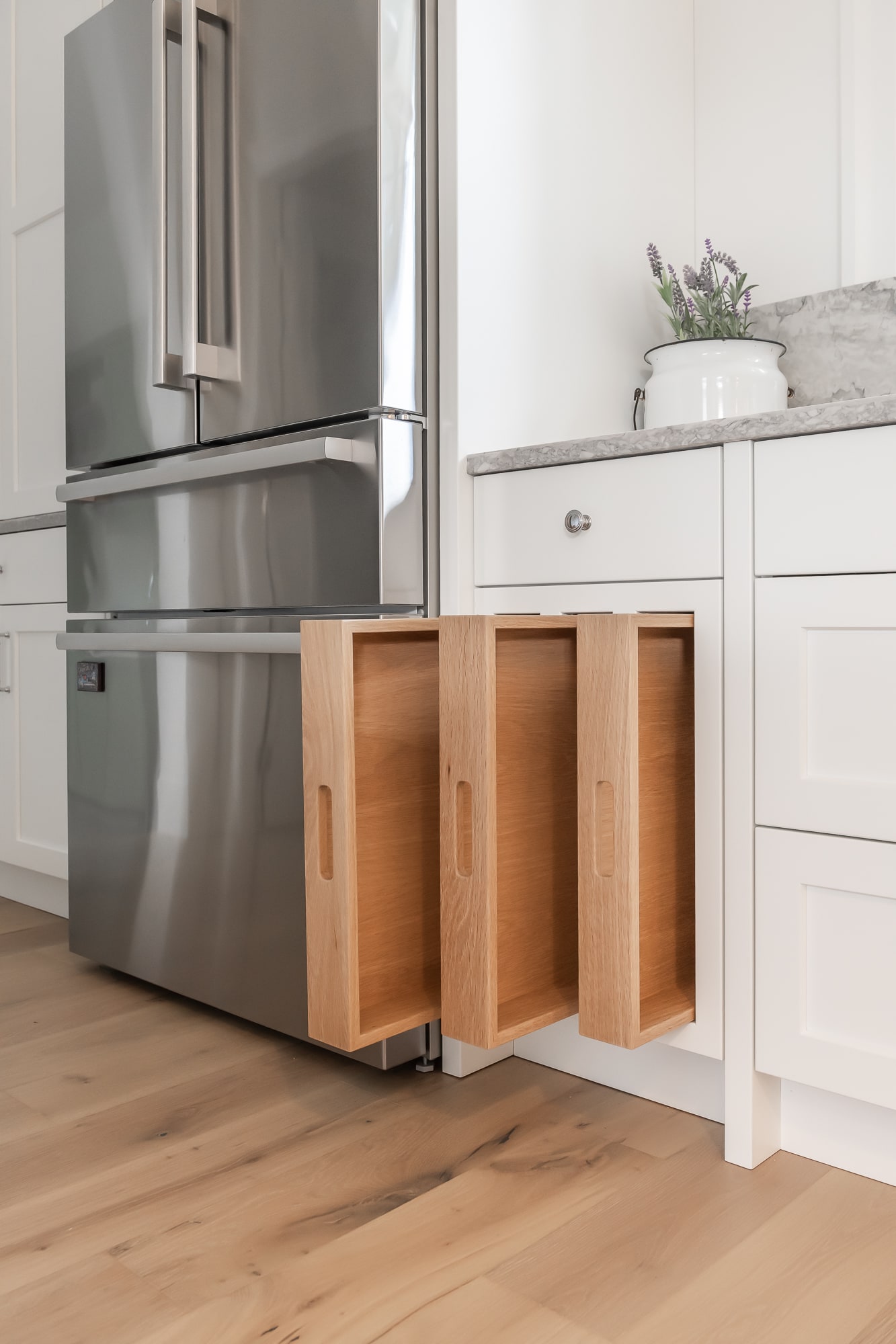 Custom kitchen cabinetry detail by Alderidge Construction showing light wood lower cabinets alongside stainless steel refrigerator with white upper cabinet pairing