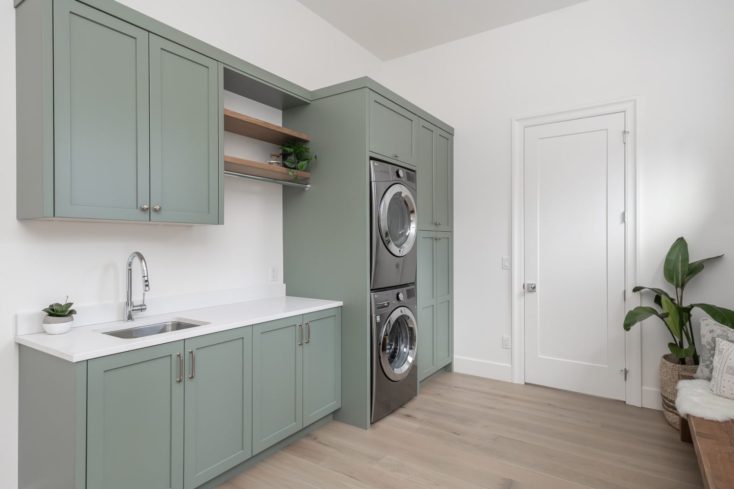 Custom laundry room with sage green shaker cabinetry, open shelving, and utility sink by Alderidge Construction, designed for functional and stylish home storage