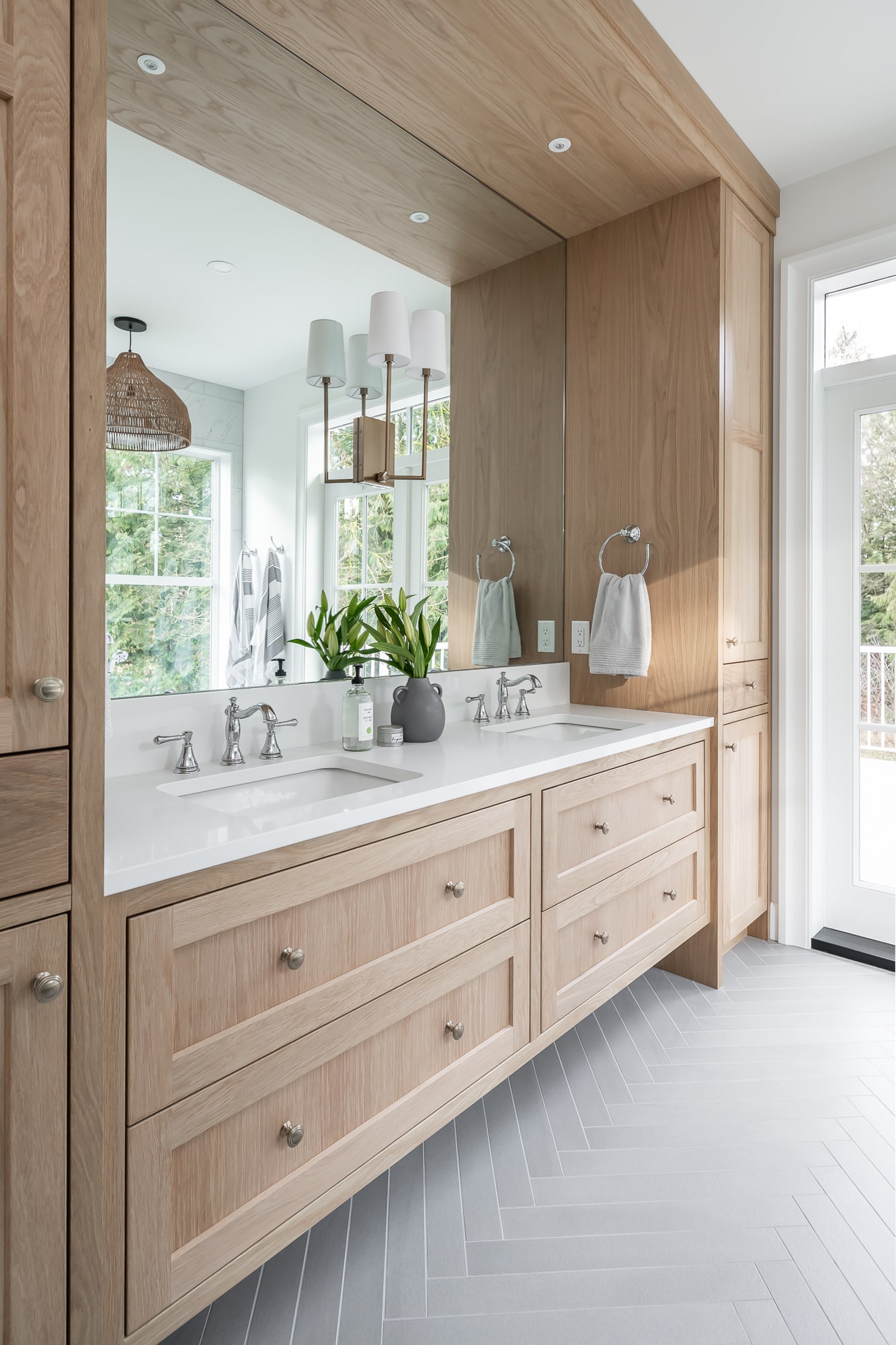 Custom light wood double bathroom vanity by Alderidge Construction with framed mirror surround, white marble countertop, and pendant lighting in a spa-style ensuite