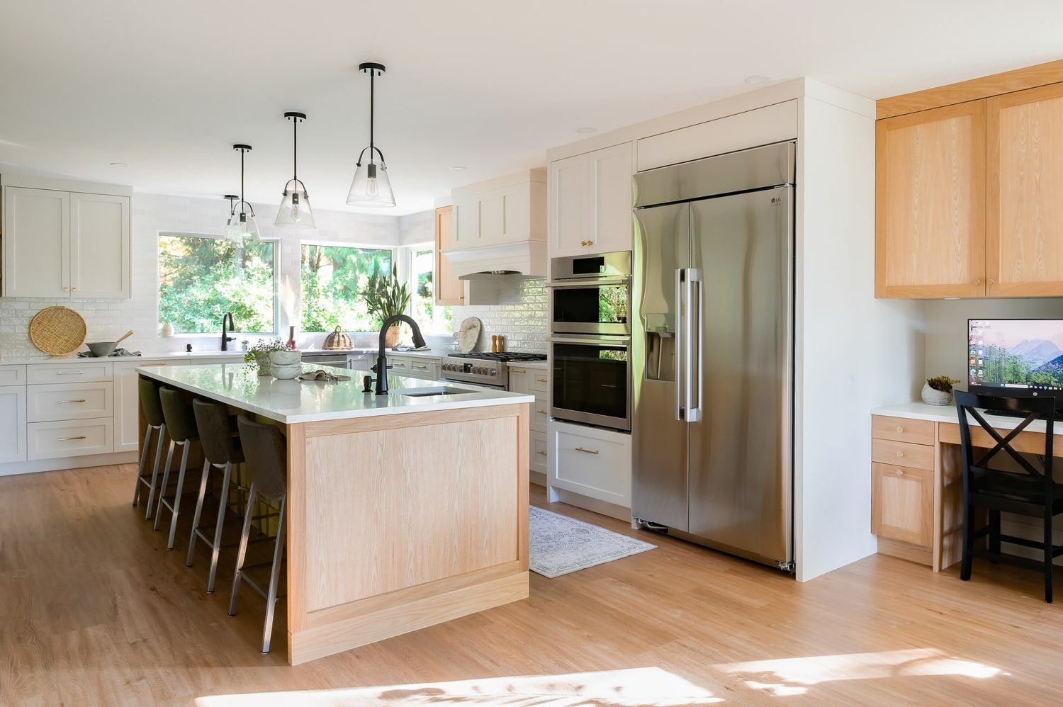 Custom kitchen cabinetry by Alderidge Construction combining white lower cabinets and natural wood uppers with stainless appliances and statement pendant lighting