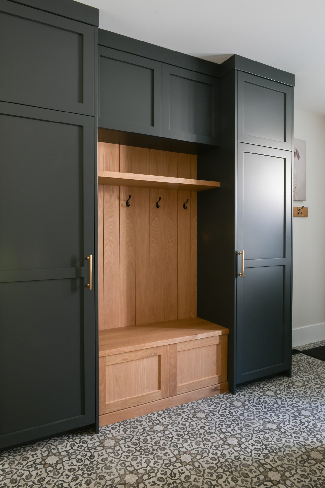 Custom mudroom cabinetry by Alderidge Construction with dark charcoal shaker doors, natural wood locker bench, and built-in coat hooks on patterned tile