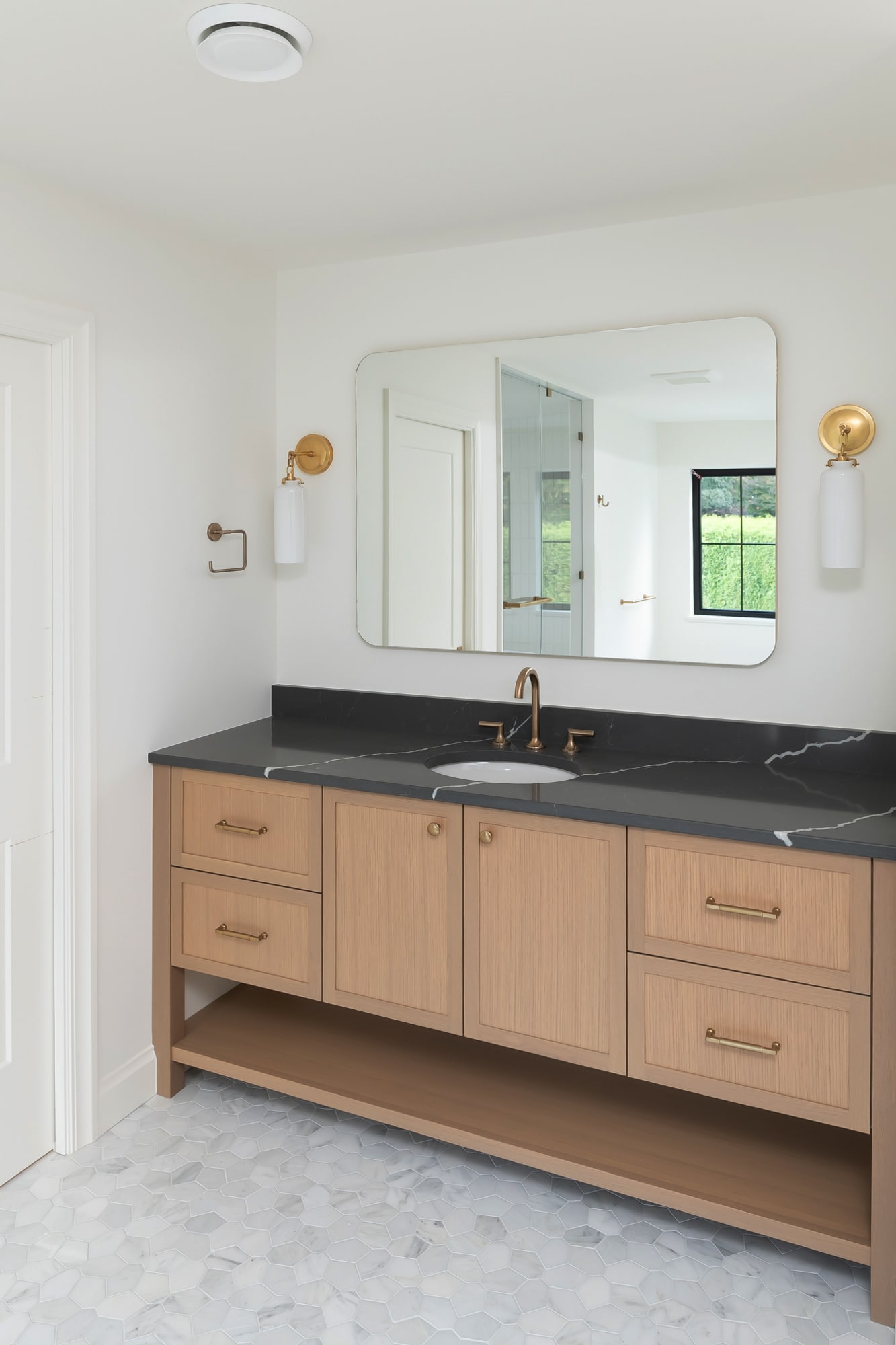 Light oak bathroom vanity with dark marble countertop, undermount sink, and brass fixtures