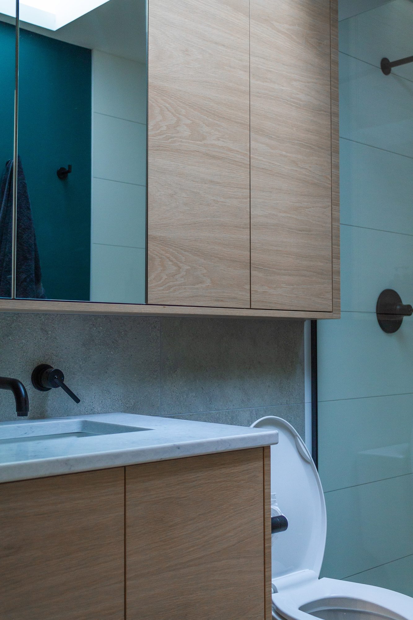 Custom bathroom vanity with natural wood-grain cabinet doors by Alderidge Construction, paired with teal tile accent wall and matte black hardware