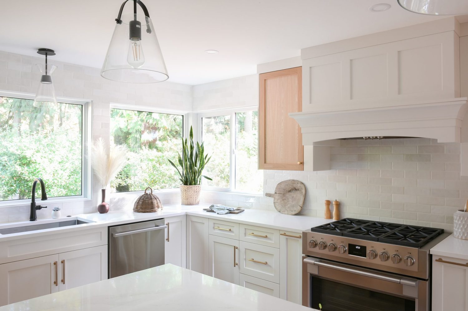 Renovated kitchen with white shaker cabinets, a custom range hood, tile backsplash and corner windows in the Shearwater renovation by Alderidge Construction